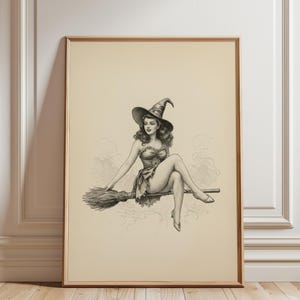 May include: A framed black and white print of a vintage-style witch riding a broom. The witch is wearing a hat and a dress, and the artwork has a classic pin-up aesthetic. The print is in a wooden frame.