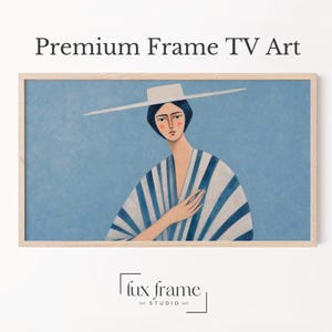 May include: A rectangular light wood frame containing digital art of a person wearing a wide-brimmed white hat and a blue and white striped garment against a blue background. The text Premium Frame TV Art and lux frame EST STUDIO 2022 are visible.