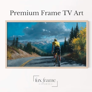 May include: A framed landscape painting depicting a cyclist on a mountain road. The cyclist wears a yellow top. The sky is blue with clouds. The frame is light brown. Text at the top reads "Premium Frame TV Art".