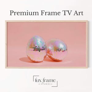 May include: A framed print featuring two disco ball egg shapes with iridescent, mirrored surfaces. The background is a solid light pink. The text "Premium Frame TV Art" is at the top.
