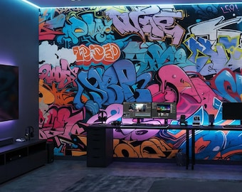 May include: A modern gaming room with a vibrant graffiti mural as a backdrop. The room features a black desk with dual monitors, a large TV, and a comfortable gray sofa. The walls are painted dark gray, and the room is illuminated with neon lights.
