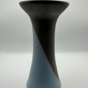 May include: A tall, ceramic vase with a flared top and a conical base. The vase is divided diagonally, with a dark brown section and a light blue section. The vase has a textured surface and a smooth rim.