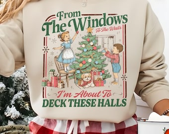 May include: Beige sweatshirt with a Christmas-themed graphic. The graphic features children decorating a Christmas tree, a dog, and the text "From The Windows To The Walls, I'm About To Deck These Halls."