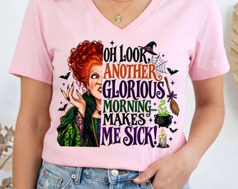 May include: A light pink V-neck t-shirt featuring a graphic of a woman with red hair in a green dress next to the text "OH LOOK, ANOTHER GLORIOUS MORNING... MAKES ME SICK!" along with illustrations of a witch hat, spider web, broom, cauldron, and candle.