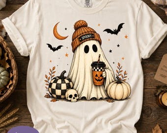 May include: An ivory short-sleeve t-shirt featuring a graphic of a ghost wearing a brown beanie with the text SPOOKY. The ghost holds a jack-o'-lantern coffee cup, flanked by a checkered pumpkin, a plain pumpkin, a skull, bats, and a crescent moon.