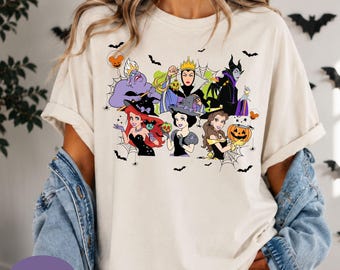 May include: An ivory t-shirt featuring a graphic print of six animated characters dressed in Halloween costumes, including witches and villains, surrounded by spider webs and small black bats. The design includes a pumpkin and mouse-shaped balloons.