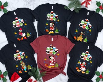 May include: A collection of Christmas-themed t-shirts featuring Disney characters. Each shirt displays a different character, including Mickey Mouse, Minnie Mouse, Donald Duck, Daisy Duck, and Pluto, with festive balloon designs and Christmas trees.