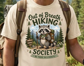 May include: Beige t-shirt with a raccoon graphic, hiking backpack, and text that reads "Out of Breath Hiking Society." The raccoon is holding a walking stick. A sign reads "Worth it (probably)."