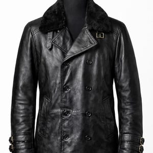 May include: A black leather coat with a double-breasted design, featuring a faux fur collar and buckle details on the sleeves. The coat has multiple buttons and a classic, tailored fit, displayed on a mannequin.