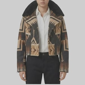 May include: A cropped jacket featuring a geometric pattern in shades of brown, tan, and charcoal gray. The jacket has a large black faux fur collar, long sleeves, and a front zipper closure. It is worn over a crisp white button-down shirt and black pants.