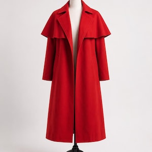 May include: A vibrant red coat with a cape-like overlay, displayed on a mannequin. The coat features a classic collar and long sleeves, reaching to the ankles. The garment is made of a smooth fabric, and the overall design is elegant and timeless.