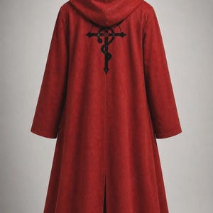 May include: A long, red hooded coat featuring a black Flamel symbol printed on the back. The coat has long sleeves, a hood, and a vertical slit at the bottom hem. The fabric has a textured, matte appearance, and the garment is displayed on a mannequin.