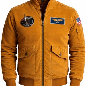 Puede incluir: Chaqueta bomber de pana color mostaza con cremallera, dos bolsillos delanteros y un bolsillo pequeño en la manga izquierda. Cuenta con parches, incluyendo una bandera estadounidense y un parche azul con alas.