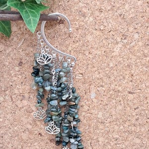 Può includere: Polso auricolare argentato con fili pendenti di piccole pietre preziose verdi e grigio-blu. Il polso ha un design curvo che si aggancia sopra l'orecchio, con piccoli ciondoli a forma di fiore di loto argentati.