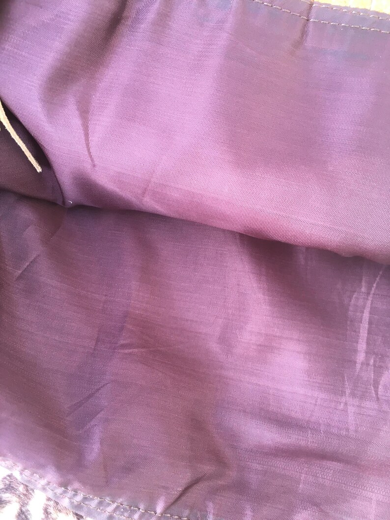 Puede incluir: Primer plano de una tela morada con un brillo sutil. La tela parece ser un material de forro, con costuras visibles en los bordes. El color es un morado profundo y apagado, con ligeras variaciones de tono.