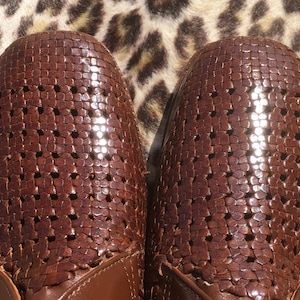 May include: Close-up of two brown leather shoes with a woven design. The shoes have a perforated pattern and a glossy finish. The shoes are set against a leopard print background.