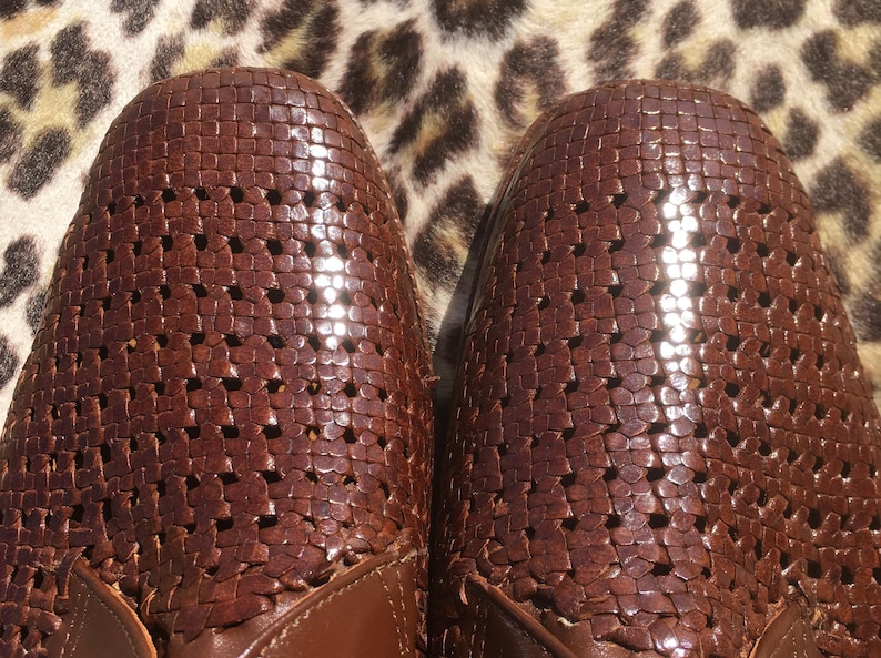 May include: Close-up of two brown leather shoes with a woven design. The shoes have a perforated pattern and a glossy finish. The shoes are set against a leopard print background.
