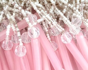May include: A decorative fringe trim featuring long, matte pink cylindrical beads and clear, faceted spherical beads. The beads are suspended from a network of small, opaque white seed beads arranged in a repeating, interconnected lattice pattern.
