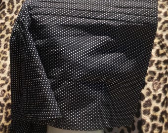 Puede incluir: Una tela negra con lunares blancos está drapeada sobre una cabeza de maniquí. La tela está doblada y plisada, creando una apariencia texturizada. El fondo presenta un estampado de leopardo.