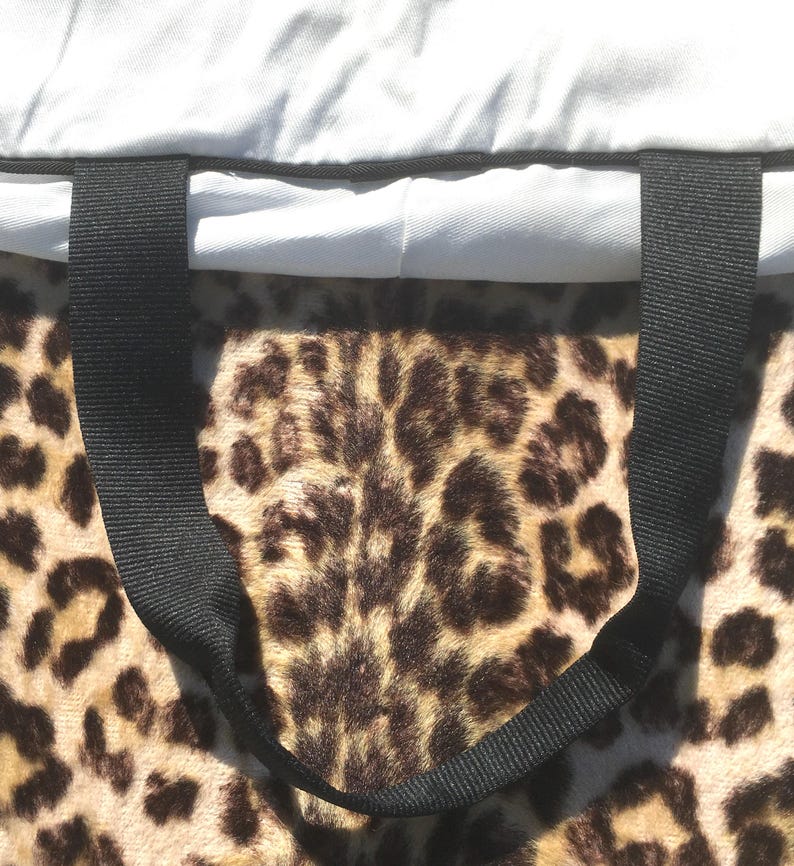 May include: A tote bag with a leopard print pattern. The bag has a black handle and a light gray top. The leopard print is brown and tan. The bag is made of a soft, plush material.