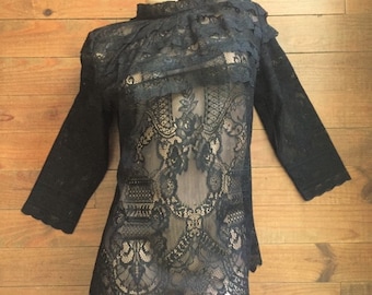 Può includere: Top in pizzo nero con collo alto e maniche lunghe. Il top ha un colletto arricciato e un design in pizzo trasparente.