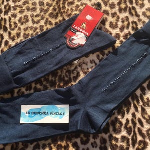 Peut inclure: Deux paires de chaussettes bleu marine avec une ligne de petits ornements décoratifs. Une paire est pliée et l'autre est dépliée. Une étiquette rouge avec la marque "LABONAL" est attachée à la paire pliée. Un autocollant avec le texte "LA DOUCHKA VINTAGE" est sur la paire dépliée.