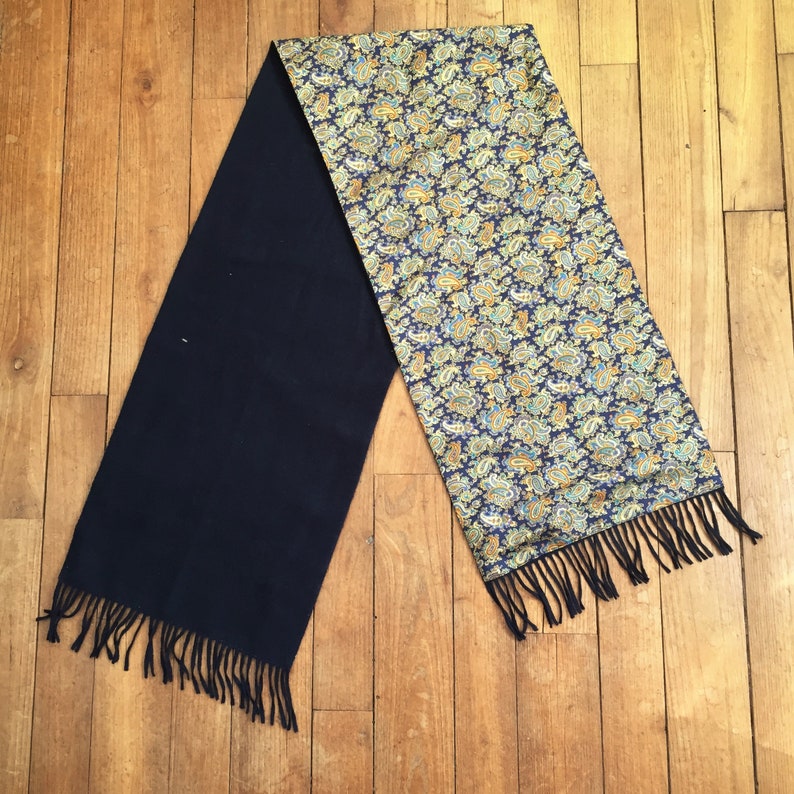 May include: A reversible scarf with a paisley pattern on one side and a solid dark blue color on the other side. The scarf has fringe on both ends.