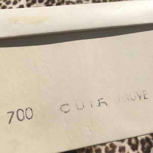 May include: A cream-colored shoe box with the number 9 and the text "700 CUIR TAUVE" printed on the side. The box is made of a textured material.
