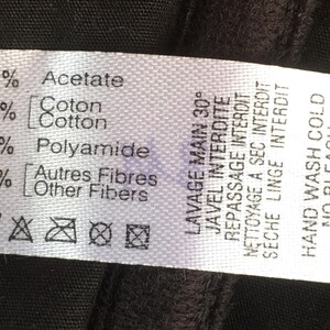 May include: A white fabric clothing label with black text detailing fabric composition: 65% Acetate, 20% Cotton, 10% Polyamide, and 5% Other Fibers. Washing instructions include hand wash cold, no bleach, no iron, no dry cleaning, and no tumble.