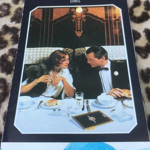 Könnte beinhalten: Eine Vintage-Werbung für den Venice Simplon Orient Express mit einem speisenden Paar. Das Bild enthält den Text "Venice Simplon Orient Express SM 1985" und "La Douchka Vintage".