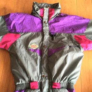 May include: A gray, purple, and pink ski suit with a diamond-shaped patch that says "Snow Jump".