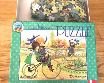 May include: A vintage "Miss Petticoat" puzzle box with a pastoral illustration of children on a bicycle and scooter. The box is green with white polka dots and contains 250 puzzle pieces. The puzzle is by Nathan.