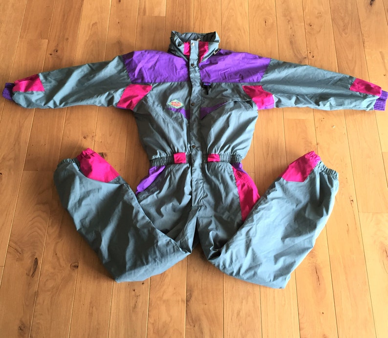May include: A gray ski suit with pink and purple accents. The suit has a zipper closure and a hood.