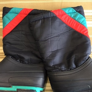 Puede incluir: Un par de botas de invierno negras con una parte superior acolchada y un patrón geométrico turquesa y rojo alrededor de la parte superior de la bota.