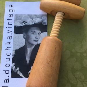 May include: A vintage wooden corkscrew with a light brown finish. The corkscrew has a spiral mechanism and a handle. A black and white image of a woman wearing a hat is in the background. The text "la.douchka.vintage" is on the image.
