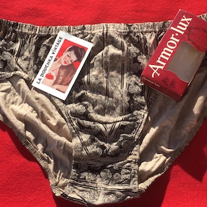 May include: Vintage underwear with a black and tan paisley pattern, a tan lining, and an elastic waistband. A tag reads "LA DOUCHKA VINTAGE" with a pin-up girl image. A red box reads "Armor-lux".
