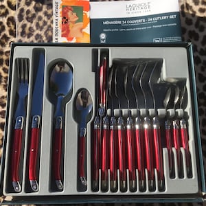 May include: A 24-piece Laguiole Heritage cutlery set in a box, featuring stainless steel utensils with glossy red handles. The set includes forks, knives, and spoons, with the box lid displaying the text Laguiole Heritage and Ménagère 24 Couverts.