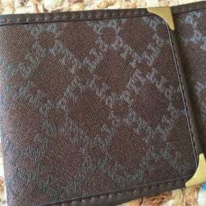 May include: A brown leather wallet with a repeating pattern of a geometric design. The wallet has a gold metal corner piece.