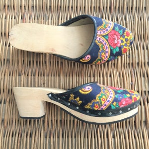 Könnte beinhalten: Ein Paar Holzclogs mit einem schwarzen und weißen Paisley-Druck. Die Clogs haben einen hohen Absatz und eine geschlossene Spitze.