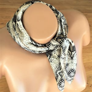 Peut inclure: Un foulard en soie à imprimé serpent blanc et noir noué autour du cou d'un mannequin.