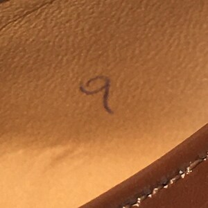 May include: Close-up of a brown leather surface with a handwritten number 9 in blue ink. The stitching of a leather item is visible in the lower right corner.