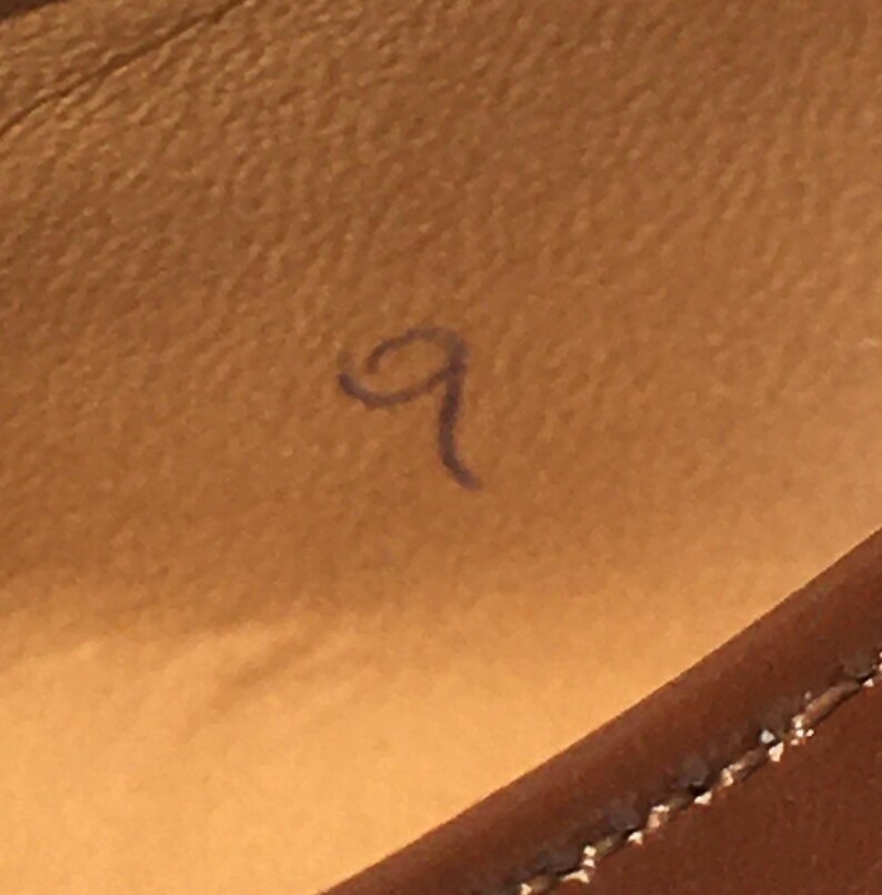 May include: Close-up of a brown leather surface with a handwritten number 9 in blue ink. The stitching of a leather item is visible in the lower right corner.