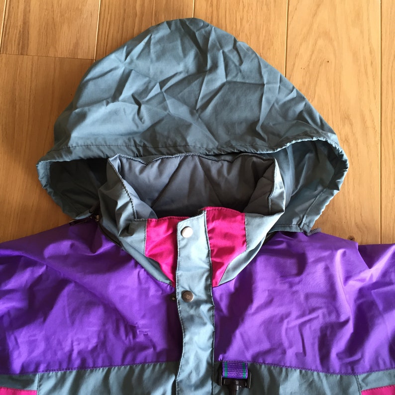 May include: A multi-colored jacket with a hood. The jacket is purple, pink, and gray. The hood is gray and has a drawstring.
