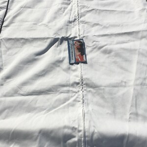 May include: A white garment bag with a black trim and a zipper closure. The bag has the brand name "VALENTINO" printed on it. A tag with the text "LA DOUCHKA VINTAGE" and an illustration is attached to the bag.