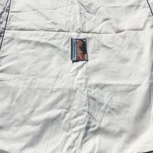 May include: A white Valentino garment bag with black trim and handles. The brand name is printed across the top. A small rectangular label with a vintage illustration is attached to the front.