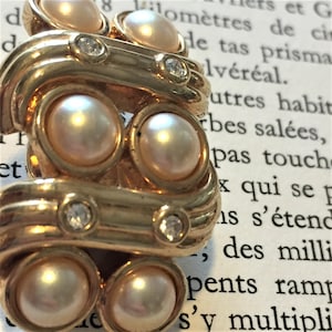 Puede incluir: Pendiente de tono dorado con cinco perlas falsas y cuatro diamantes de imitación transparentes. El pendiente está diseñado en forma de onda.