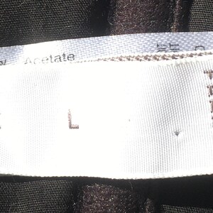 May include: Close-up of a white clothing label with the text "SIZE L" and "MADE IN FRANCE". The label is on a dark fabric. The fabric is made of Acetate.