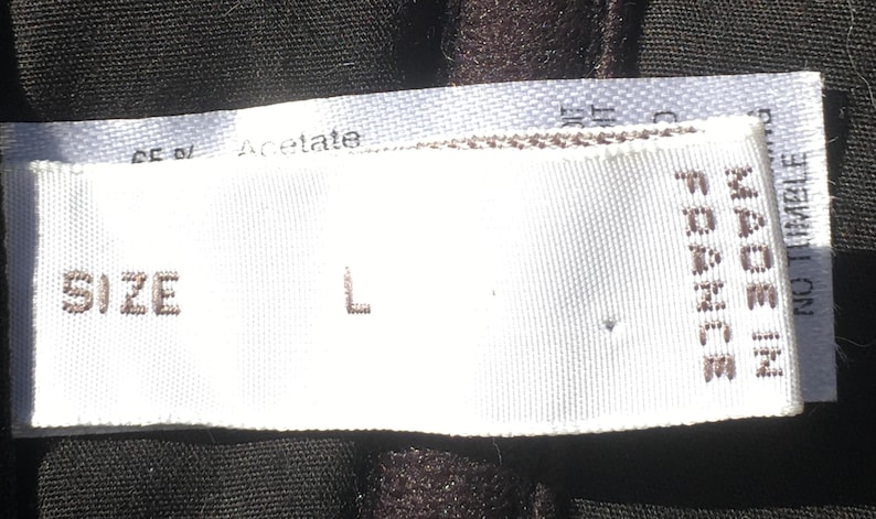 May include: Close-up of a white clothing label with the text "SIZE L" and "MADE IN FRANCE". The label is on a dark fabric. The fabric is made of Acetate.