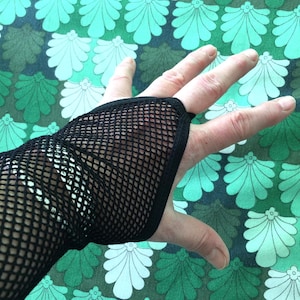 May include: Black fishnet fingerless glove. The glove is made of a black mesh material and covers the hand up to the knuckles. The background features a pattern of green and white floral shapes.