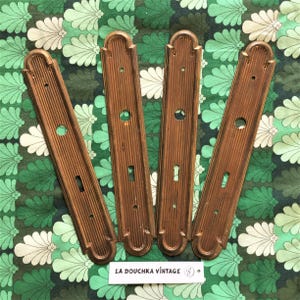 Pode incluir: Quatro placas de porta de latão antigo com um design decorativo e canelado. Cada placa tem uma fechadura e uma parte superior arredondada.